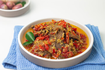 Dendeng Balado, Indonesian traditional beef cuisine from Padang, West Sumatra with slices beef cooked with some spices and a lot of chilies. Served on ceramic plate and isolated white background.   