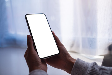 Mockup image of a woman holding mobile phone with blank white desktop screen