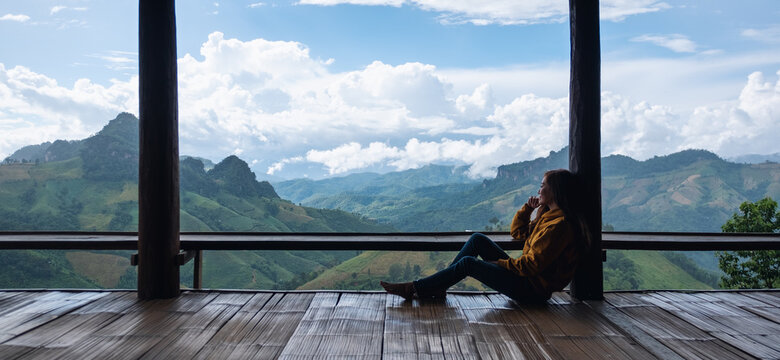 A female traveler sitting and looking at a beautiful mountains and nature view on wooden balcony