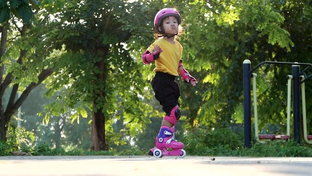 Little girl wearing protection pads and safety helmet learning to roller skate in summer park. Active outdoor sport for kids.