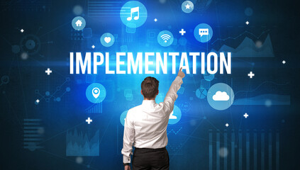 Rear view of a businessman with IMPLEMENTATION inscription, modern technology concept