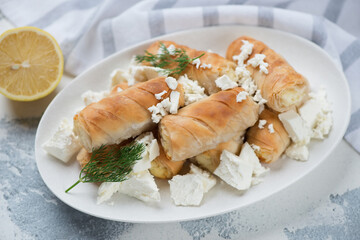 White oval plate with greek mini feta rolls, horizontal shot on a white concrete surface