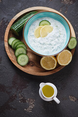 Bowl of greek tzatziki or cucumber yogurt sauce on a round wooden serving tray, top view on a brown stone background, vertical shot