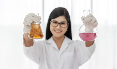 Young Asian scientist woman holding and looking at the chemical flasks in the laboratory	