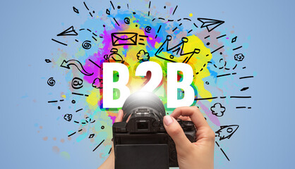 Close-up of a hand holding digital camera with abstract drawing and B2B inscription