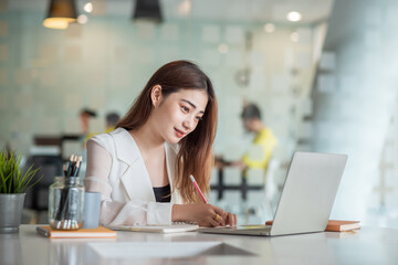 Pretty and charming asian businesswoman sitting happily smiling with laptop computer in the office.