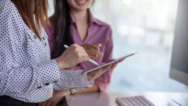 Two Young Business Woman Using Digital Tablet In The Conversation, Exchanging Ideas At Work.