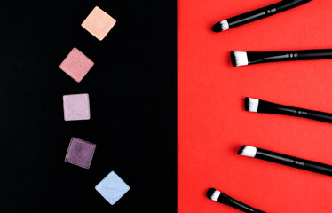 Eyeshadows of different colors and black makeup brushes on a black and red background. Black and red background with cosmetics