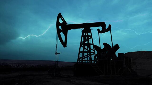 The machine for pumping oil and gas works at night during thunderstorms and lightning. Silhouette of a working oil pump from an oil field against the night sky with bright flashes of lightning.