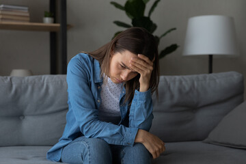 Unhappy young Caucasian woman loner outcast sit on couch at home missing thinking. Upset sad female feel distressed depressed, suffer from loneliness or lack of communication. Solitude concept.