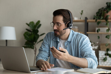 Young Caucasian man in earphones sit at desk in home office have online video training or meeting...