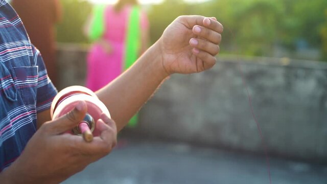 Slow motion shot of man holding a charki phirki thread spool in the crook of his elbow and winding it with the other hand to ensure taughtness for the famed kite fighting festival of makar sankranti