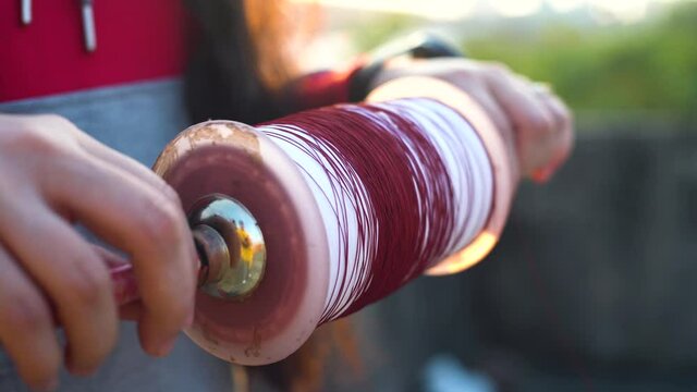 shot of girl lady woman using both hands to wind string on a charkhi spool for kite flying with different colors for the saddi plain thread and red for the glass covered manjha for kite fighting