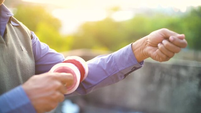 Slow motion shot of man holding a charki phirki thread spool in the crook of his elbow and winding it with the other hand to ensure taughtness for the famed kite fighting festival of makar sankranti