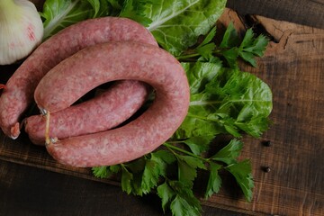 Sausage ring, garlic, chard and parsley sprigs,red chili on  wooden board on wooden table background.Meats and Sausages.Top view. Homemade natural sausage.