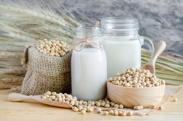 Homemade organic soybean milk in glass bottle with some dry seeds in sack and wooden bowl over blur...