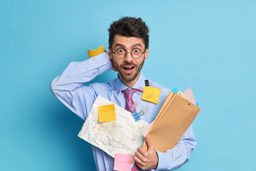 Surprised unshaven man employee prepares startup project works with papers has deadline to prepare...