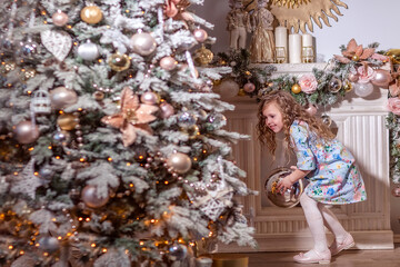 A beautiful laughing girl with curly long hair stands near a decorated Christmas tree. Decorates the Christmas tree.