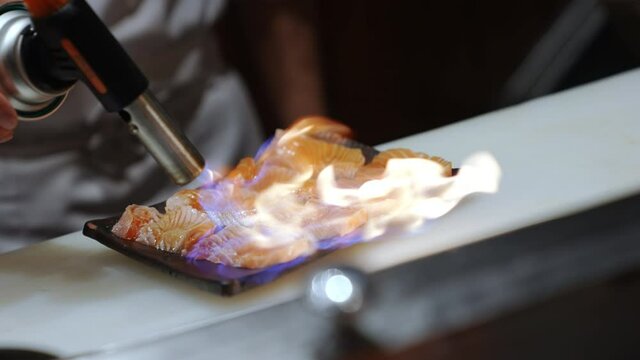 Professional male chef burning sliced salmon meat on the plate for preparing delicious healthy food menu burned salmon rice bowl or aburi salmon ikura donburi on kitchen counter in japanese restaurant