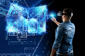 A man in virtual reality glasses designs a building a hologram of a house. Construction,...