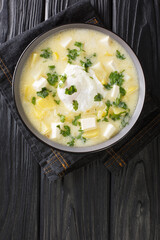 Pisca Andina is a soup usually made with chicken broth, diced potatoes and eggs, then garnished with white cheese and cilantro close-up in a bowl on the table. Vertical top view from above