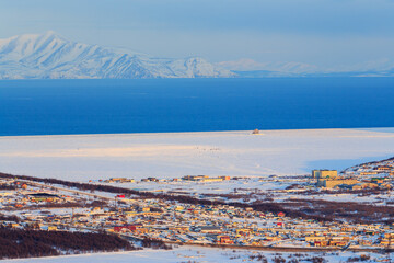 Aerial photography of the coast of the sea bay. Town by the sea. The sea is partially covered with ice. Mountains in the distance. Suburb of Magadan, Magadan Region, Far East Russia. Sea of Okhotsk.