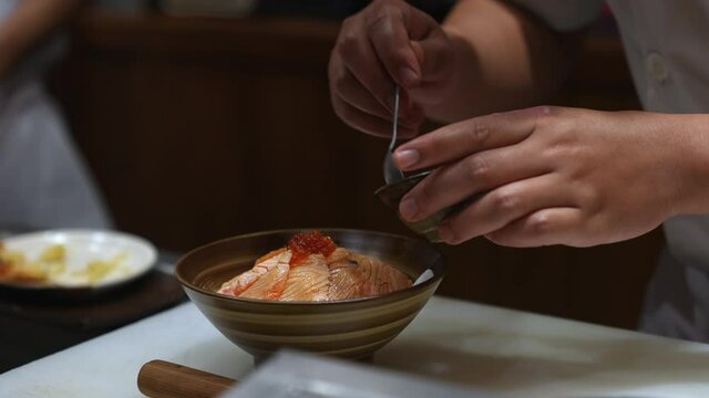 4K Close up hand of Professional chef decorate burned slice salmon rice bowl on kitchen counter. Male chef preparing delicious healthy food fish menu aburi salmon ikura donburi in japanese restaurant