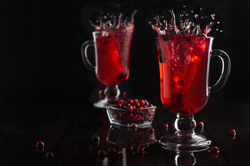Red berries tea with splash in two glasses wine glass with ripe berry in dark elegant black interior, copy space.