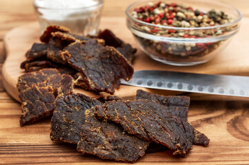 Beef jerky with salt and pepper on cutting board. Dried meat with spices.