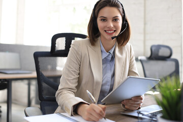 Cheerful female manager sitting at office desk and performing corporate tasks using wireless connection on digital gadgets.