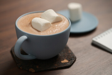 Hot chocolate in a blue cup with marshmallow and notepad on walnut table