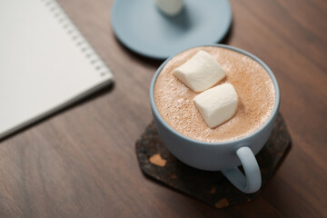 Hot chocolate in a blue cup with marshmallow and notepad on walnut table
