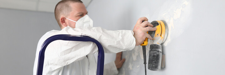 Male builder in uniform cleans wall with putty. Quality putty surfaces. Man removes an old putty...
