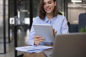 Attractive smiling woman working on a tablet in modern office.