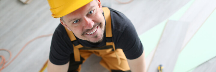 Smiling carpenter in helmet sawing laminate flooring. Simple and popular layout option. Protective...