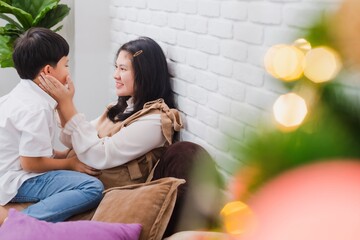 Asian pregnant mother and son sitting together at home with with Christmas tree.Concept of maintaining health during a happy pregnancy.