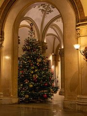 Elegantly decorated and perfectly shaped Christmas tree in an old gothic Building.  the gold colours of the ornaments fit perfectly with the hue of the old stone walls.