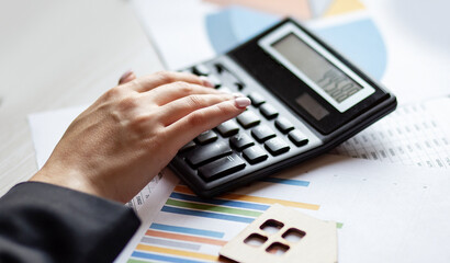 Woman calculating receipts lying on chart with wooden house