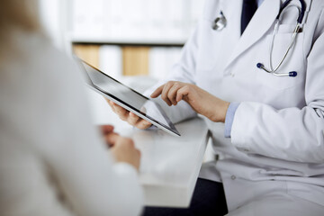 Unknown male doctor and patient woman discussing current health examination while sitting in clinic...