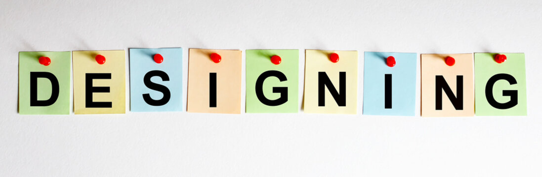 DESIGNING phrase is written on multi-colored stickers, on the white background. Business concept, strategy, plan