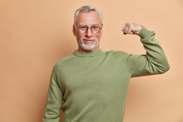 Confident satisfied grey haired man raises arm and shows muscle demonstrates results after regular...
