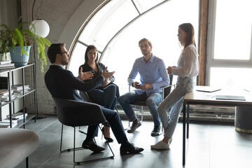 Concentrated millennial male ceo leader setting targets to staff workforce members on daily briefing in modern office, young business partners colleagues sitting in circle planning teamwork on meeting