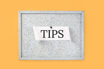 Tips word on a grey cork notice board on orange background. Top tips or quick advice concept