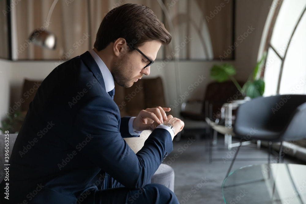 Poster Time management. Serious male employee looking at wrist watch checking time waiting for hr invitation on job interview, punctual young businessman expecting partner who is late for meeting in office