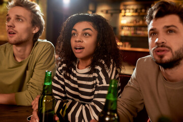 Friends in the bar watching sports match on TV together, drinking beer and cheering for team. People, leisure, friendship and entertainment concept