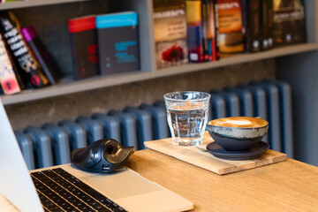 Cozy remote working morning in cafe - cup of delicious cappuccino coffee, protection mask, laptop on desk and books