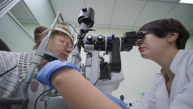 Woman doctor is viewing through ophthalmoscope in eyes of patient in ophthalmologic clinic. Professional inspection of vision