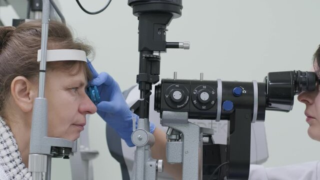 Woman doctor is viewing through ophthalmoscope in eyes of patient in ophthalmologic clinic. Professional inspection of vision