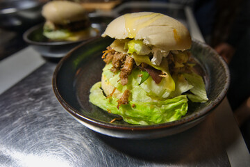 Pulled Pork Beef Burger auf einem schwarzen Tonteller mit Salat und Käse