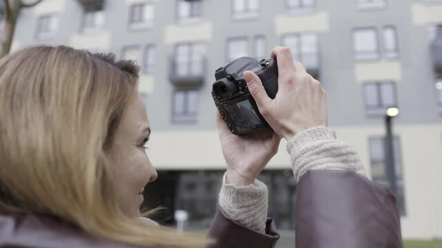 Close up of female photographer taking pictures of a multi storey residential building. Action. Side view of a professional camera in hands of a female.